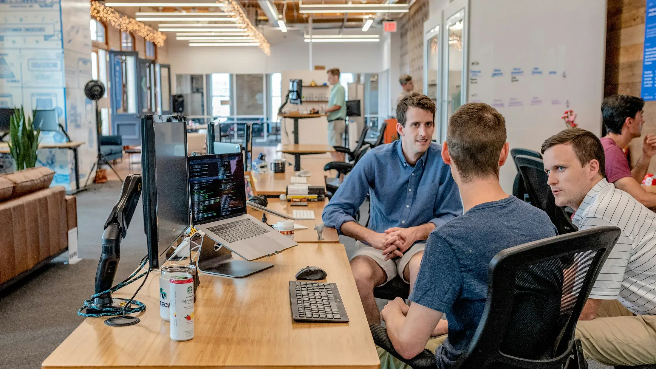 Équipe d’ingénierie échangeant autour d’un poste de travail avec code et notes de conception.
